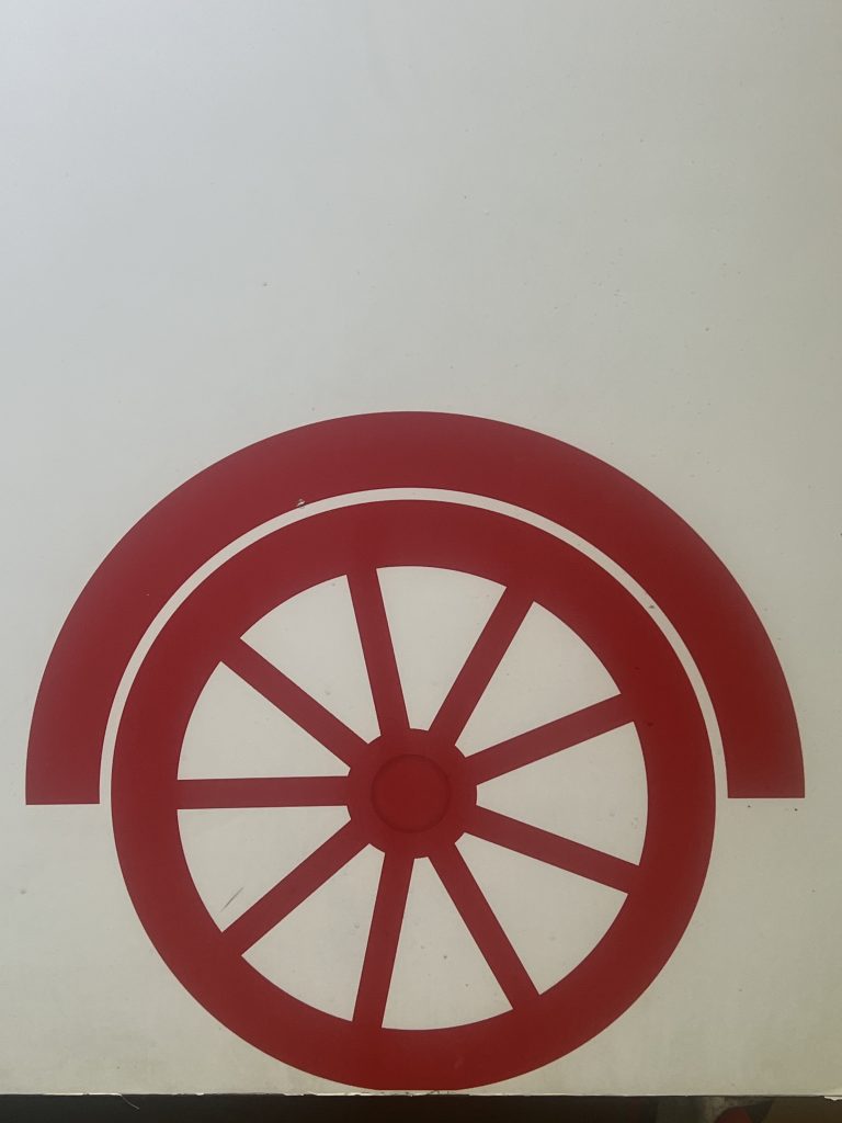 A simple red graphic of a wagon wheel with a curved fender on a plain white background.