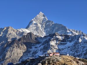 Fishtail Mountain rising sharply against a clear blue sky, with rocky slopes and snow-capped peaks.
