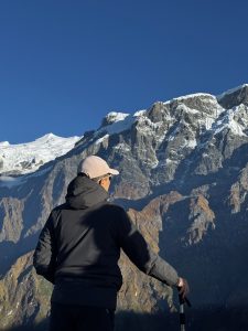 
A person stands with their back to the camera, looking out over a dramatic mountain landscape.
