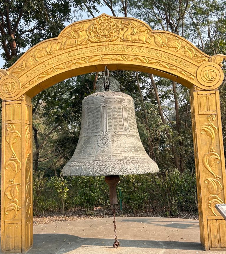 A large, ornate bell hangs from a golden-yellow arch adorned with intricate carvings and floral motifs.