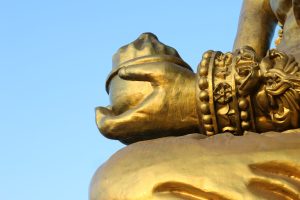 
A close-up of a golden statue's hand, which holds a small bowl or pot.