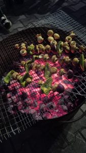 Grilled vegetables, including mushrooms and green bell peppers, arranged on a wire grill above glowing charcoal, with a dark background and some visible reflections of light
