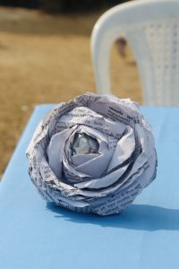 A decorative flower made from crumpled pieces of newspaper, placed on a blue table.