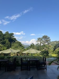 
A scenic view showing a vibrant blue sky with a few white clouds. In the foreground, there are dark wooden tables and chairs arranged outside. 