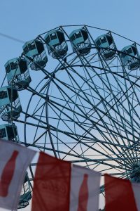 A large Ferris wheel with turquoise cabins is prominently featured against a clear blue sky. 