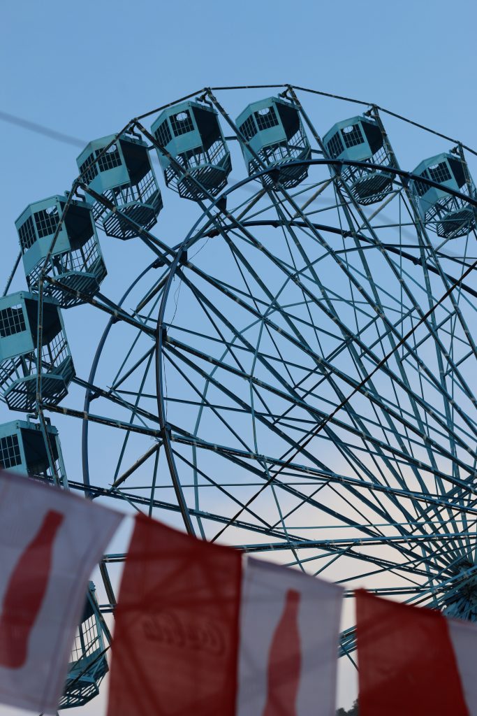 A large Ferris wheel with turquoise cabins is prominently featured against a clear blue sky.