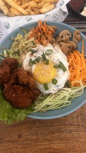 A blue bowl with fresh vegetables, mushrooms, and a fried egg on top.