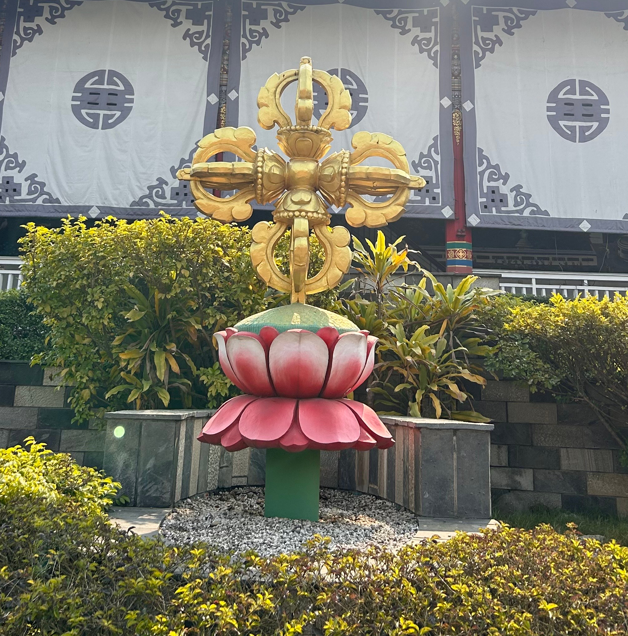 A large decorative structure stands in a garden, featuring a vibrant red and pink lotus flower base with broad petals.