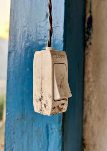 A close-up of a slightly dirty white light switch hanging from a twisted wire.