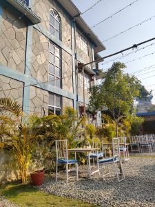 A cozy outdoor seating area is set against a backdrop of a building with textured stone walls painted in light blue.