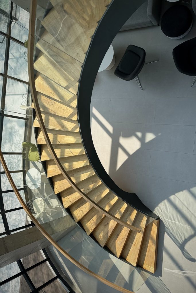 An aerial view of a spiral staircase featuring wooden treads and a glass railing