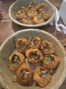 A close-up image of two bowls made from leaves, each containing pani puri—round, hollow crispy shells filled with a flavorful mixture of diced onions, fresh herbs, and spices.