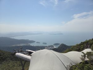 Panoramic high viewpoint with canopy, green mountains descending to a blue bay with boats and islands.