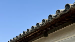Close-up of a traditional Japanese roof in Kurashiki, showing layered ceramic kawara tiles and decorative round end caps under a clear blue sky.

