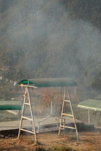 A swing set with a green canopy sits on a grassy area, surrounded by mist, with trees and hills partially hidden in the background.