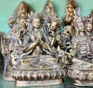 
A collection of intricately designed metal statues of various deities, predominantly showing a central figure seated in a meditative pose with hands in a prayer position. 