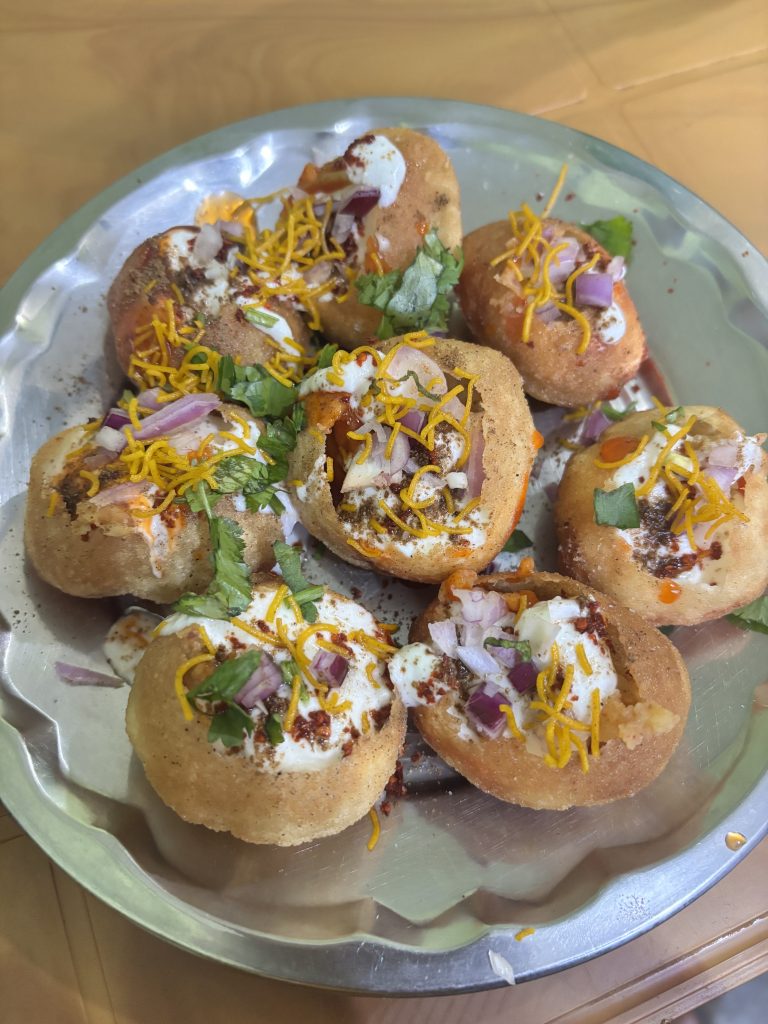 A silver plate of dahi puri—crispy hollow shells filled with spiced potatoes.