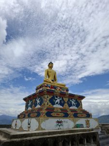 A large golden statue of a seated Buddha is positioned on a decorative pedestal adorned with intricate patterns. 