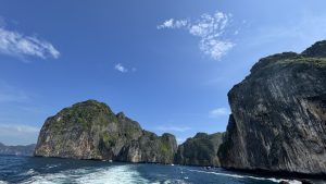 
A panoramic view of steep, rocky cliffs covered in lush greenery, rising sharply from the turquoise sea.