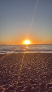 A calm beach at sunset, with the sun glowing on the horizon and golden light reflecting on gentle ocean waves in Chile.