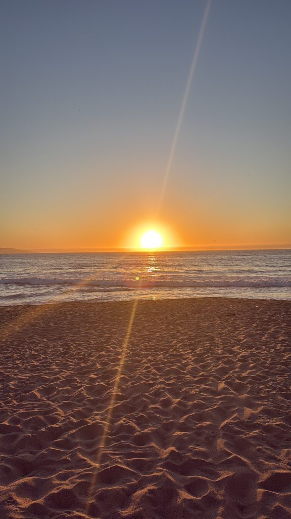 A calm beach at sunset, with the sun glowing on the horizon and golden light reflecting on gentle ocean waves in Chile.