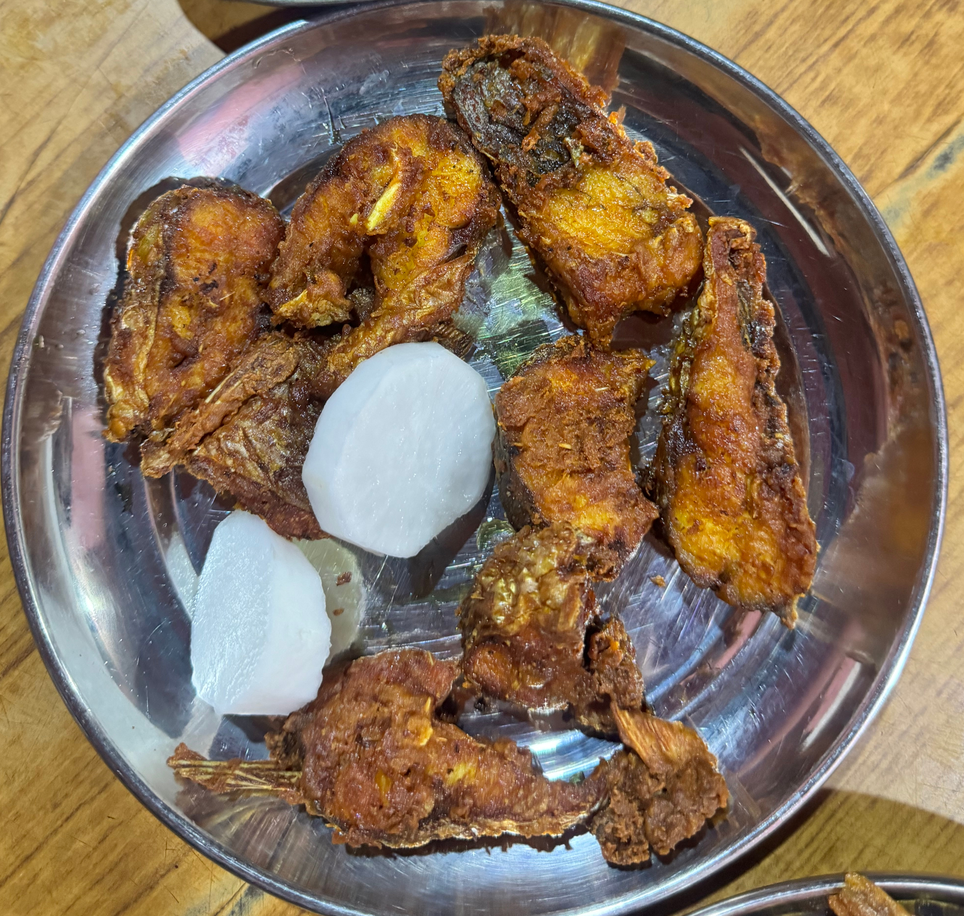A round metal plate filled with several pieces of fried fish that appear golden brown and crispy.