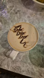 Closeup of the top of a cup of coffee with foam on top.  The pattern like a tall plant.