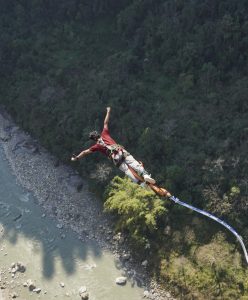 A person is bungee jumping over a river, surrounded by green trees, with arms spread wide and enjoying the thrill.