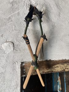 A slingshot with wooden X-shaped handle and a dark rubber band hangs on a white wall.
