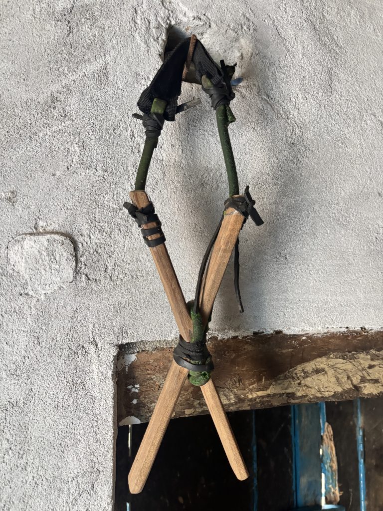 A slingshot with wooden X-shaped handle and a dark rubber band hangs on a white wall.