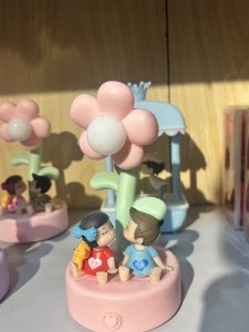 
A close-up of a decorative figurine featuring two cartoonish children, a girl and a boy, sitting on a pink base.