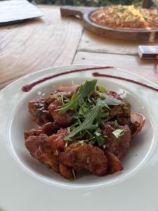Close-up of Chicken Chilli with fried chicken pieces in spicy red sauce, topped with fresh green herbs.