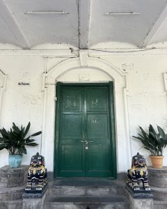 A green double door with a padlock set in an aged white wall.