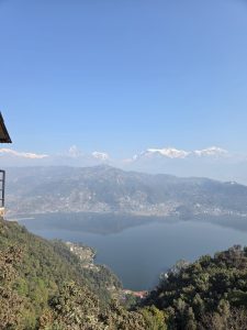 


A panoramic view of a serene mountainous landscape featuring a large, calm Fewa lake at the forefront. 