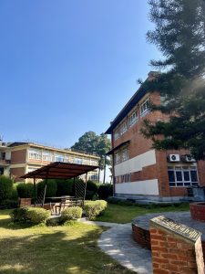 
A view of a landscaped area featuring two buildings, one made of red brick and the other with a light facade