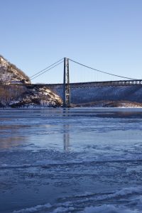 The Bear Mountain Bridge over an icy Hudson River with a blue sky in the background.