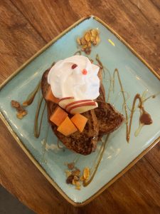 Thick slices of French toast are topped with whipped cream and diced fruit on a light blue plate.