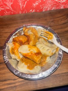 A small aluminum foil dish filled with steaming dumplings topped with a savory orange sauce.