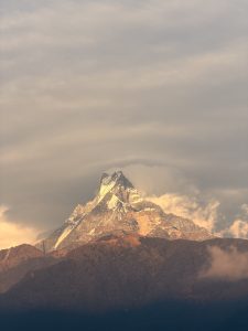 


A majestic Fishtail mountain peak rises dramatically against a cloudy sky, its summit capped with snow.