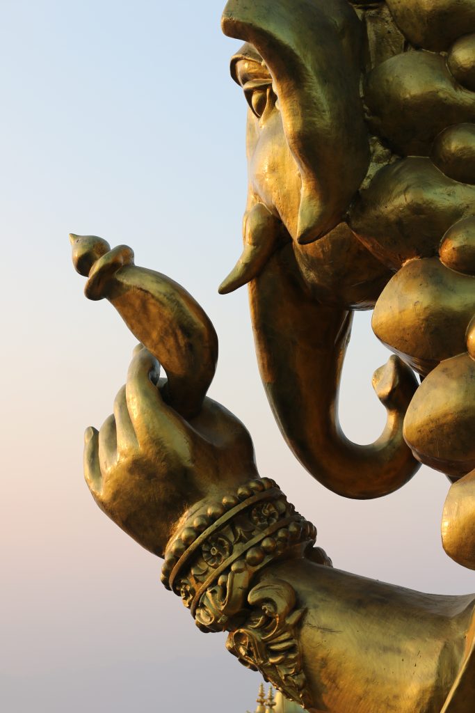 A close-up of God Ganesh’s golden hand holding a modak, adorned with ornate bracelets and decorations.