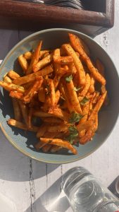 A close-up view of a bowl filled with golden-brown seasoned French fries, garnished with small pieces of fresh cilantro. 