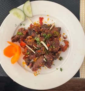 A white plate holds a colorful dish featuring pieces of cooked meat, diced vegetables, and herbs.