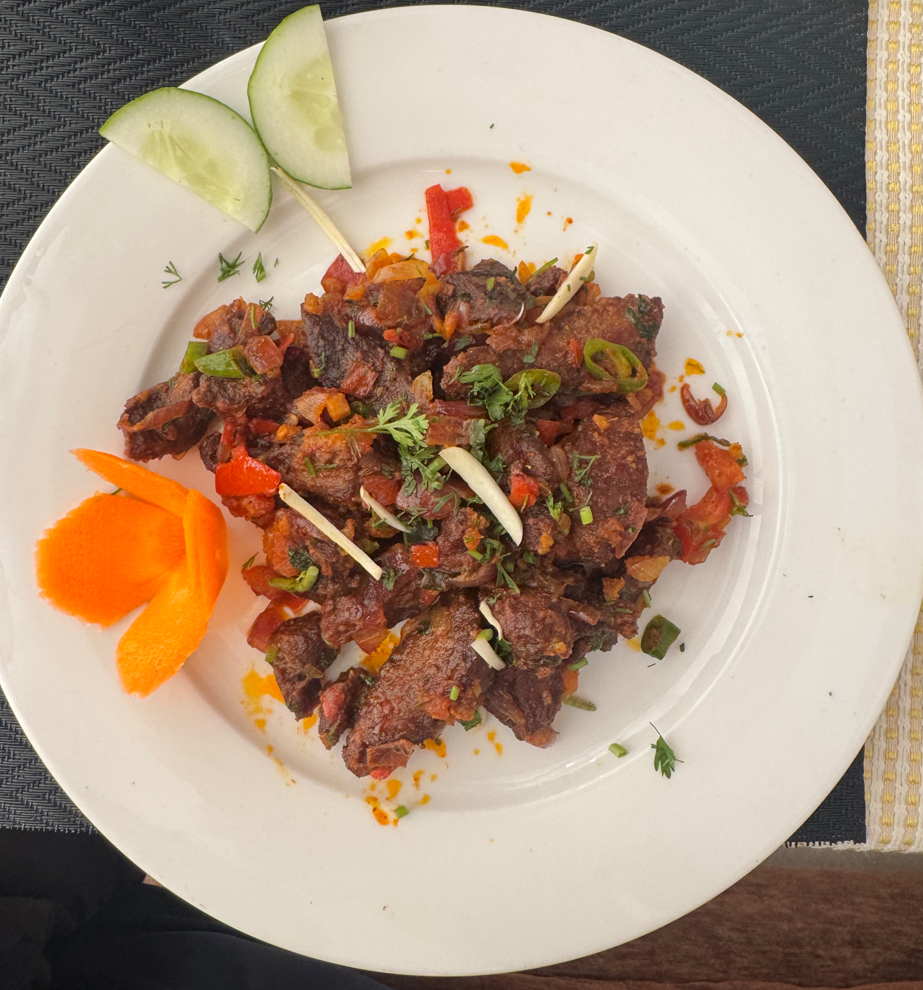 A white plate holds a colorful dish featuring pieces of cooked meat, diced vegetables, and herbs.