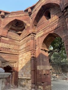 Red sandstone structure with intricate carvings, arches, greenery, and a blue sky.