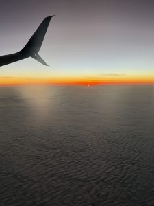 
A sunset view from an airplane window, with the silhouette of the airplane's wing in the foreground. 