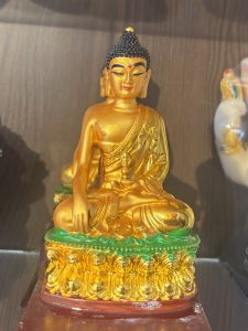 
A golden statue of a seated Buddha with a serene expression, wearing a draped robe.