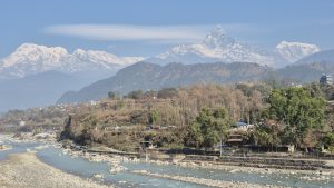 
A panoramic view of snow-capped mountains in the background, with a blue sky above and wispy clouds. 