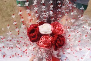 
A close-up view of a bouquet featuring several handmade flowers in various shades of red and white, wrapped in clear plastic with white and red floral design patterns.