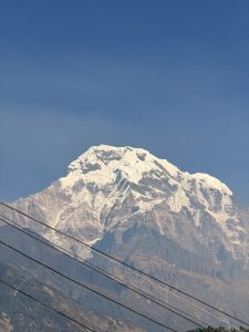 A majestic snow-capped mountain dominates the scene, rising sharply against a clear blue sky. 