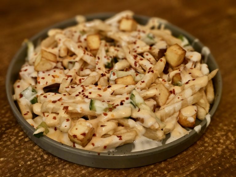 Close-up of cheesy French fries with sauce, chili flakes, paneer, and small toppings in Kozhikode, Kerala, showing the texture and flavour clearly.
